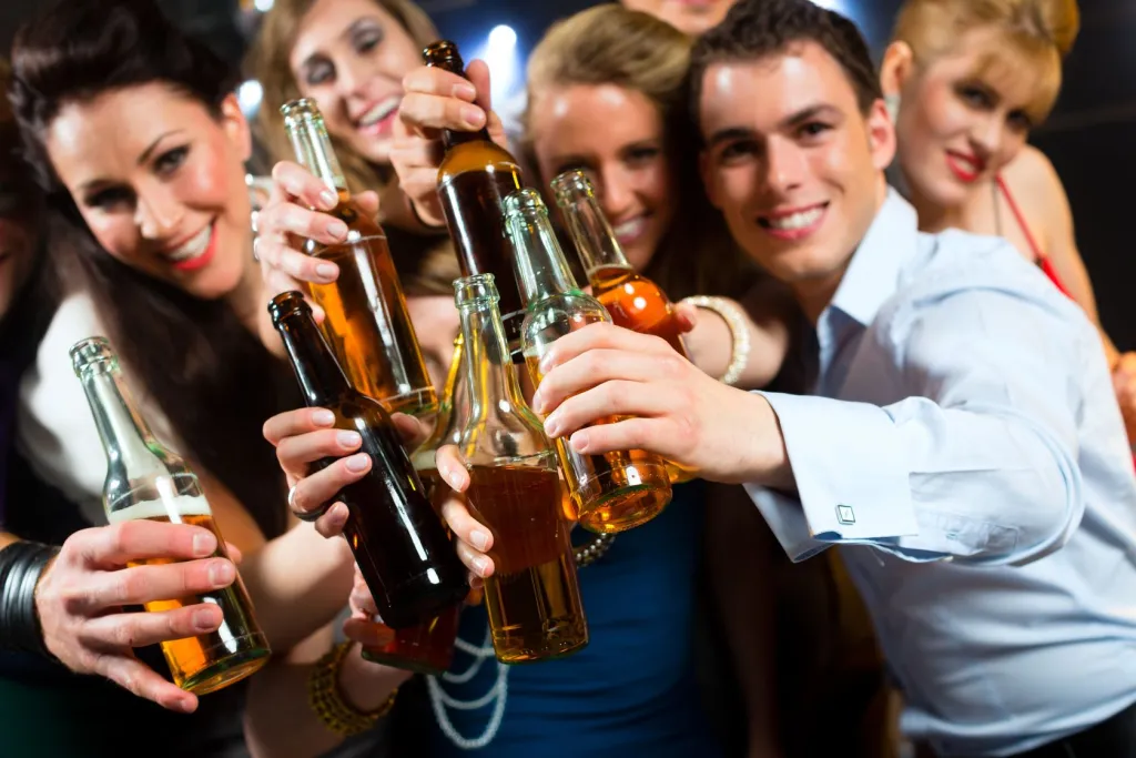 young people in club or bar drinking beer out of a beer bottle and have fun