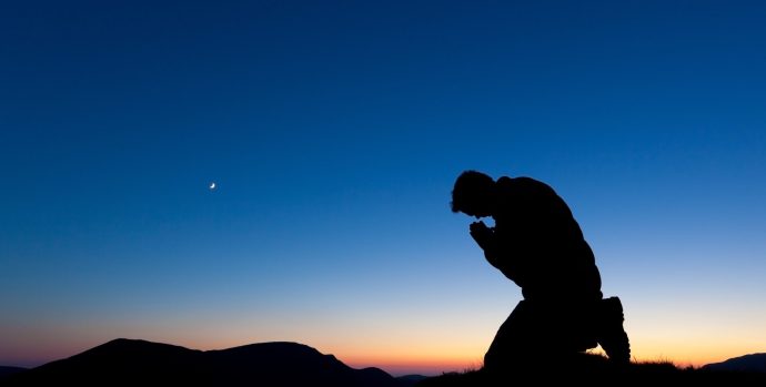 Man praying on the summit of a mountain at sun set with the moon in the sky.