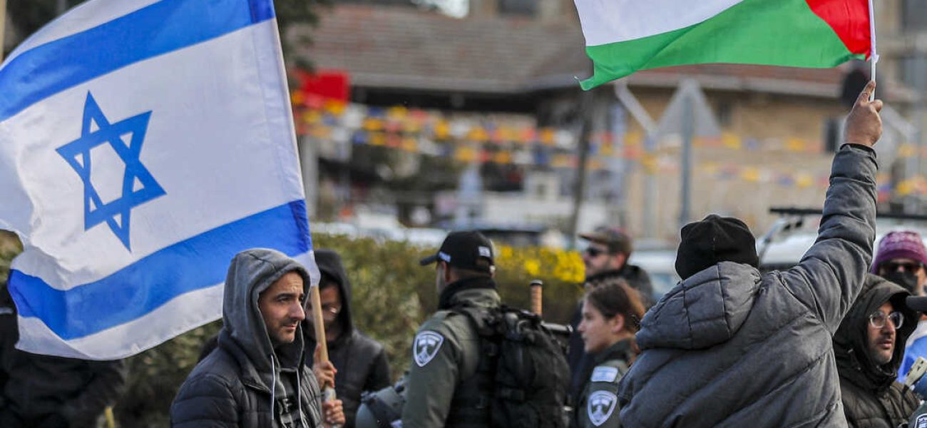 An Israeli settler stands with an Israeli flag before a man holding up a Palestinian flag during a demonstration attended by Palestinians, Israelis, and other foreign activists in the east Jerusalem neighbourhood of Sheikh Jarrah on February 25, 2022, denouncing the evacuation of Palestinian families from their homes and settlement activity in the Palestinian Territories and east Jerusalem. - Israel captured east Jerusalem in the Six-Day War of 1967 and later annexed it, in a move not recognised by the international community. More than 200,000 Jewish settlers have since moved into the city's eastern sector, fuelling tensions with Palestinians, who claim it as the capital of their future state. (Photo by AHMAD GHARABLI / AFP) (Photo by AHMAD GHARABLI/AFP via Getty Images)