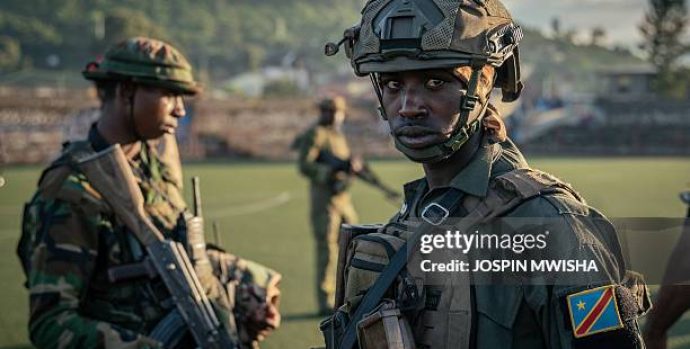 An M23 soldier watches over a group of around one hundred Democratic Forces for the Liberation of Rwanda (FDLR), Wazalendo and Armed Forces of the Democratic Republic of the Congo (FARDC) fighters, at the Stade de l'Unité, during their presentation by Colonel Willy Ngoma in Goma on May 10, 2025. These fighters were previously neutralised by the AFC/M23 security services. (Photo by Jospin Mwisha / AFP) (Photo by JOSPIN MWISHA/AFP via Getty Images)