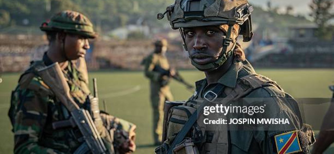 An M23 soldier watches over a group of around one hundred Democratic Forces for the Liberation of Rwanda (FDLR), Wazalendo and Armed Forces of the Democratic Republic of the Congo (FARDC) fighters, at the Stade de l'Unité, during their presentation by Colonel Willy Ngoma in Goma on May 10, 2025. These fighters were previously neutralised by the AFC/M23 security services. (Photo by Jospin Mwisha / AFP) (Photo by JOSPIN MWISHA/AFP via Getty Images)