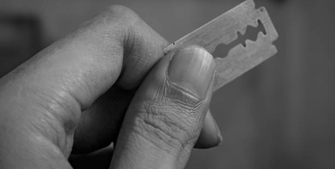 Close up of a hand holding a sharp razor blade