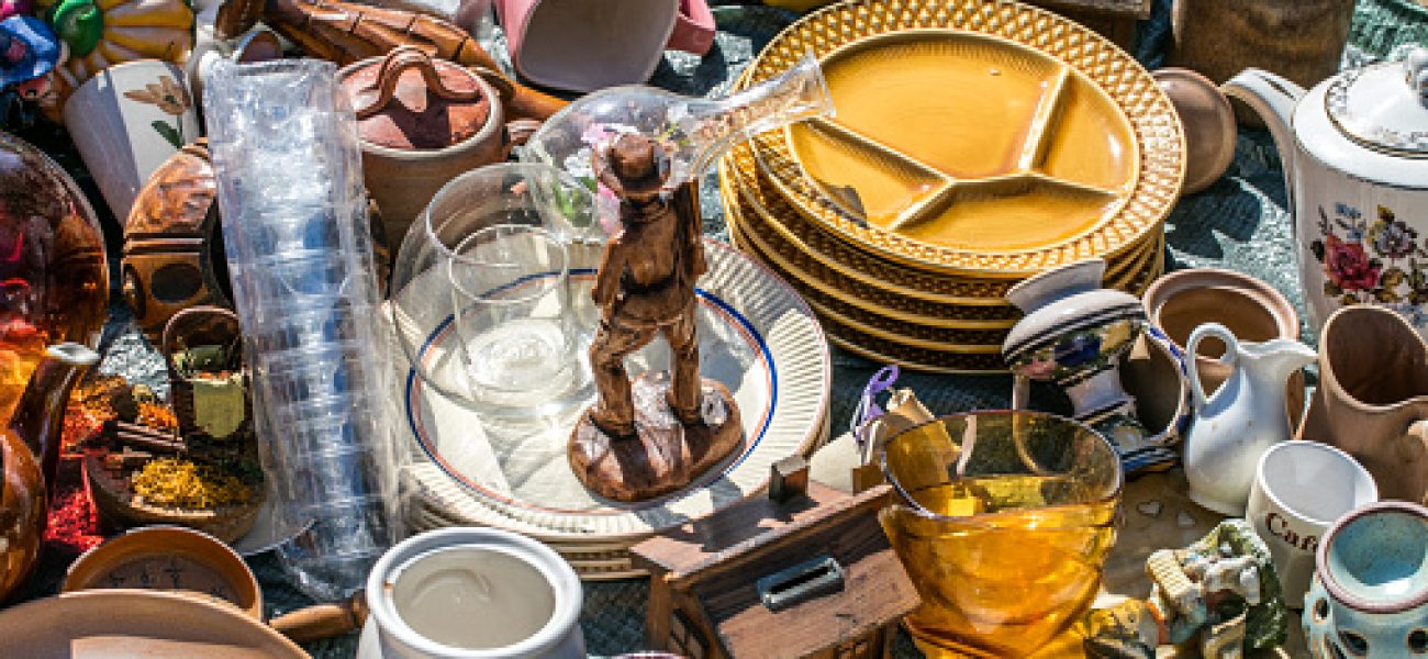 pile of household things, various dishes and decorative objects at boot sale for second hand, recycling or over-consumption society at outdoor welfare